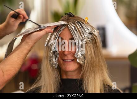 Friseur macht Foliensträhnen bei einer jungen Frau. Il parrucchiere strizza i capelli di una giovane donna Foto Stock