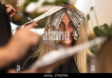 Friseur macht Foliensträhnen bei einer jungen Frau. Il parrucchiere strizza i capelli di una giovane donna Foto Stock