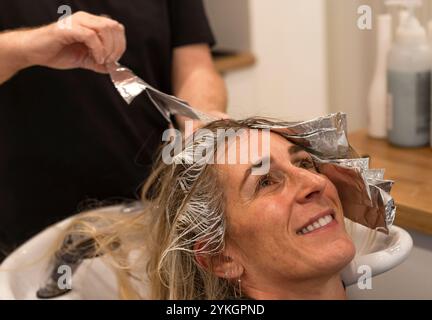 Friseur macht Foliensträhnen bei einer jungen Frau. Il parrucchiere strizza i capelli di una giovane donna Foto Stock