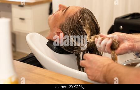 Friseur macht Foliensträhnen bei einer jungen Frau. Il parrucchiere strizza i capelli di una giovane donna Foto Stock