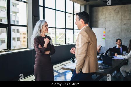 Due colleghi discutono idee in un ufficio moderno con grandi finestre Foto Stock