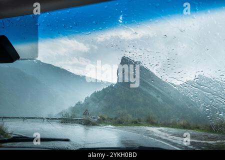 Una strada bagnata in una giornata nuvolosa e piovosa vista dall'interno di un veicolo. C'è una curva pericolosa con bassa visibilità. Concetto di guida, trasporto e Foto Stock