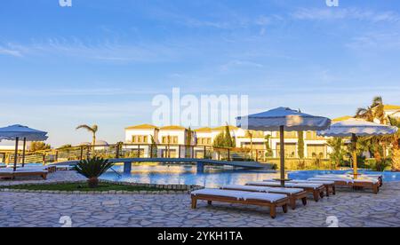 Resort e spiagge di lusso con lettini e ombrelloni nei paesaggi naturali costieri dell'isola di Kos in Grecia con cielo blu Foto Stock