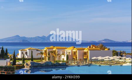 Resort e spiagge di lusso con lettini e ombrelloni nei paesaggi naturali costieri dell'isola di Kos in Grecia con cielo blu Foto Stock