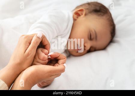 Amorevole mamma nera che tiene addormentata la mano del bambino indoor, fuoco selettivo Foto Stock