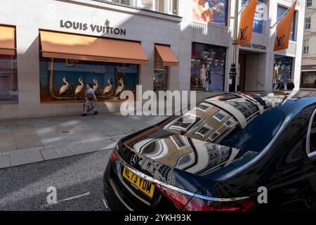 Persone che interagiscono con vetrine all'esterno del negozio Louis Vuitton in Bond Street il 7 ottobre 2024 a Londra, Regno Unito. Bond Street è una delle strade principali del quartiere dello shopping del West End ed è molto elegante. E' stata una strada di shopping alla moda dal XVIII secolo. Il ricco e ricco negozio qui, principalmente per la moda di lusso e gioielli. Foto Stock