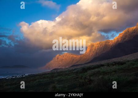 La luce del tramonto illumina le scogliere di Risco de Famara che si affacciano sulla spiaggia di Famara, Lanzarote, Isole Canarie Foto Stock