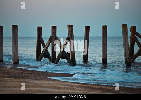 Tramonto su un vecchio molo sulla spiaggia con parco eolico sullo sfondo. Foto Stock