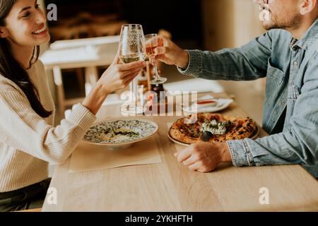 Una coppia solleva i bicchieri con un brindisi gioioso, sorridendo l'un l'altro su un rustico tavolo di legno adornato da piatti vivaci, creando un caldo e io Foto Stock