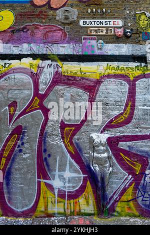 Street art lungo Brick Lane, Londra, che mostra la creatività e la diversità culturale della strada. con segnali stradali in due lingue Foto Stock