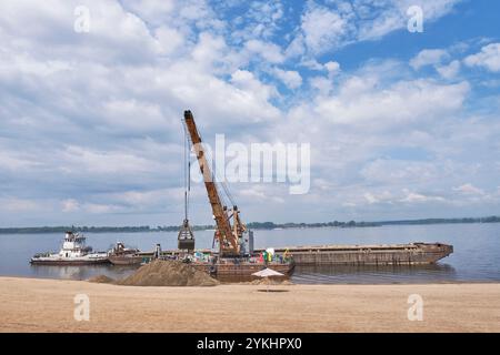 Chiatta con gru sul fiume Volga scarica sabbia sulla spiaggia sabbiosa Foto Stock