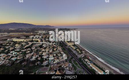 Questo presenta una vista costiera, che mostra un'area residenziale sulla spiaggia accanto a un corpo d'acqua. La scena è illuminata dalle sfumature delicate del tramonto Foto Stock