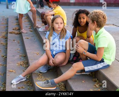 I tweenager positivi si fanno baffare mentre si siedono sui gradini all'aperto Foto Stock