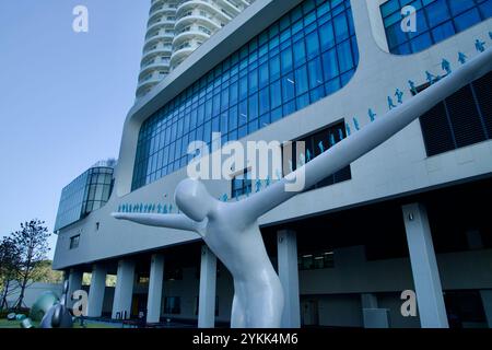 Sokcho, Corea del Sud - 3 novembre 2024: Una scultura contemporanea con braccia allungate si erge di fronte al Cassia Sokcho Hotel, che fonde modernità Foto Stock