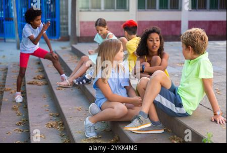 I tweenager positivi si fanno baffare mentre si siedono sui gradini all'aperto Foto Stock