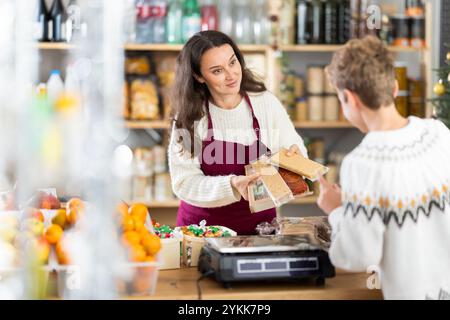 Il venditore donna serve un cliente adolescente, dimostra varie versioni di torrone e dolci natalizi. Foto Stock