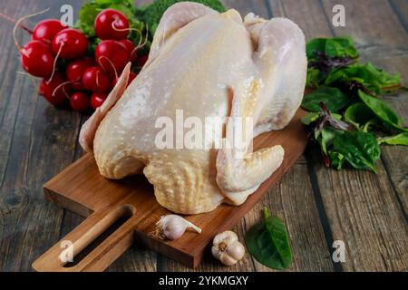 Pollo intero fresco preparato per cucinare insieme a verdure e aglio su un tagliere di legno Foto Stock