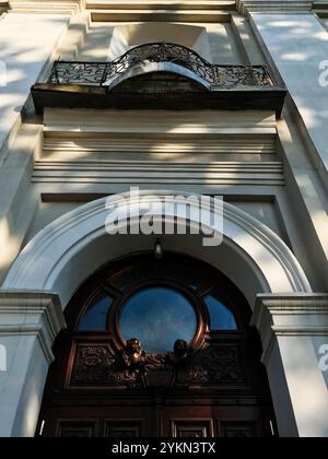 Un ingresso architettonico classico caratterizzato da intricate incisioni e un design ad arco, completato da un balcone in ferro battuto sopra. Luce solare e ombre Foto Stock