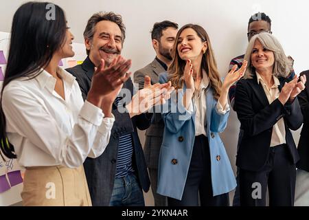Team aziendale entusiasta e diversificato che applaude e celebra il successo negli uffici moderni, colleghi multiculturali che condividono momenti di gioia mostrando inclusioni Foto Stock