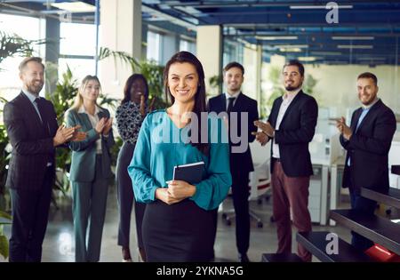 Splendida donna d'affari sorridente, leader speaker al briefing con un team eterogeneo felice in un ufficio moderno Foto Stock