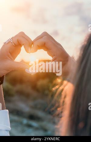 Hands Heart Sunset - la donna forma il cuore con le mani davanti al tramonto. Foto Stock