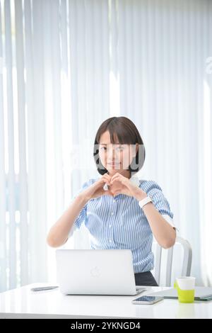 Lavoratrice che fa un segno di cuore con le mani Foto Stock