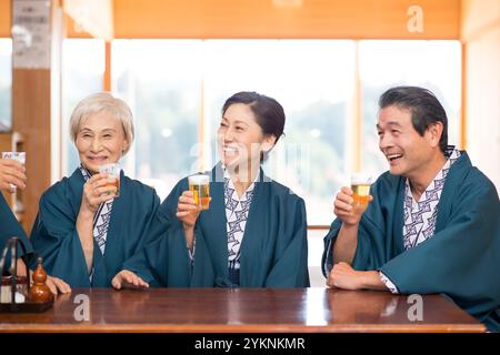 Una coppia di mezza età in yukata e haori che brinda con birra e i nonni Foto Stock