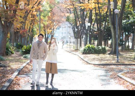 Una coppia sui vent'anni passeggiando lungo un viale alberato alla fine dell'autunno. Foto Stock