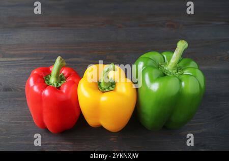 Peperoni tricolori vivaci allineati su sfondo in legno Foto Stock