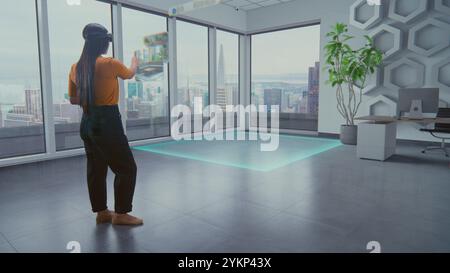 La talentuosa designer asiatica di cuffie per realtà aumentata utilizza un software di interior design virtuale per organizzare eleganti appartamenti o uffici con mobili e attrezzature 3D. Animazione futuristica VFX. Foto Stock