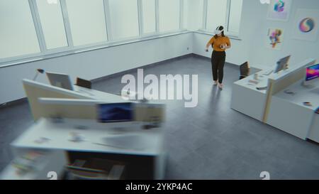 La designer asiatica creativa che indossa un visore per la realtà aumentata utilizza software e controller di interior design virtuale per costruire una stanza da ufficio con mobili e attrezzature 3D. Animazione futuristica VFX. Foto Stock