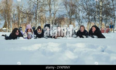 Gli amici di scuola giacciono nella neve e spruzzano neve l'uno sull'altro. Foto Stock