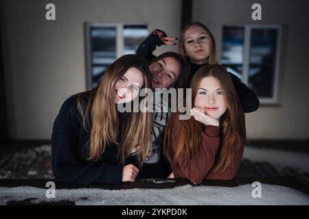 Quattro studentesse felici che posano su un tavolo coperto di neve durante un servizio fotografico invernale, divertendosi insieme Foto Stock