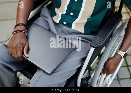 Vista dall'alto dell'irriconoscibile uomo afroamericano con disabilità che tiene un computer portatile e siede nello spazio per le copie su sedia a rotelle Foto Stock