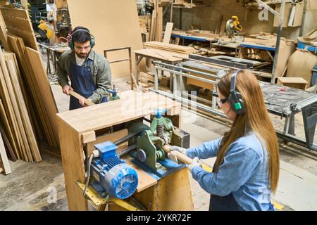 Un lavoratore più giovane e più anziano collabora in un bosco, operando macchinari e realizzando legno. La scena enfatizza il lavoro di squadra, la condivisione delle competenze e un professionista Foto Stock