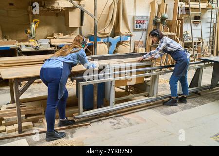 Due donne collaborano in modo efficiente in un bosco, mettendo in evidenza il lavoro di squadra e l'apprendistato. La scena mostra i moderni processi di lavorazione del legno in atto Foto Stock