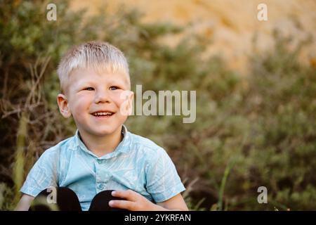 Ragazzo caucasico felicissimo seduto con la vegetazione sullo sfondo ad Albufeira, Algarve - Portogallo Foto Stock