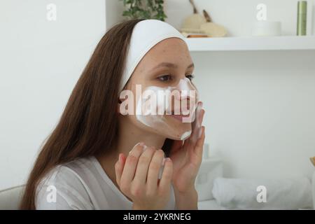 Adolescente con schiuma detergente sul viso a casa. Trattamento dell'acne Foto Stock