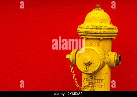 Vecchio idrante giallo di fronte al muro di cemento rosso a Japonski Island, Sitka, Alaska, Stati Uniti. Foto Stock