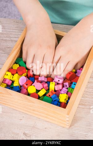 Filo da gioco per bambini in età prescolare e perline colorate in legno utilizzate per realizzare braccialetti. Sviluppo delle capacità motorie dei bambini, coordinamento, creatività e logica Foto Stock