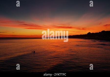 Un Surfer in the Sea a Golden Hour con Un tramonto che guarda lungo Bournemouth Beach, la costa verso Branksome Chine e Poole, Regno Unito Foto Stock