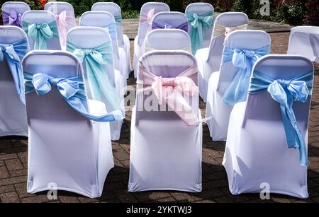 Sedie per matrimoni decorate con Bows per una cerimonia di matrimonio. Le sedie sono ricoperte di bianco con grandi fiocchi di nastro legati dietro la schiena. Foto Stock