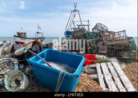 Attrezzature da pesca sulla spiaggia di Hastings, tra cui una rete in una scatola blu, vasi di aragosta e granchio, corde e due barche da pesca Foto Stock