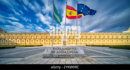 L'immagine cattura l'iconico Hospital de las Cinco Llagas, ora il Parlamento dell'Andalusia, a Siviglia. Tre bandiere ondeggiano in modo prominente sotto un vivido sk Foto Stock