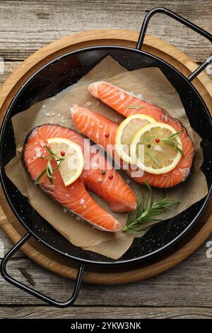 Bistecche di salmone crude fresche con spezie in padella su un tavolo di legno, vista dall'alto Foto Stock