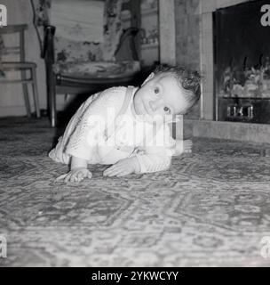 anni '1960, storico, un bambino che strizza sul pavimento di un soggiorno di fronte al fuoco di carbone che guarda in alto. Foto Stock