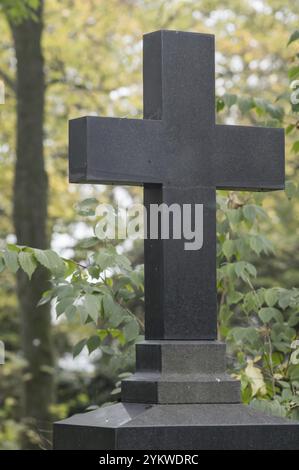 Semplice croce di pietra scura in un cimitero, che simboleggia il ricordo, la fede e il ciclo di vita e di morte Foto Stock