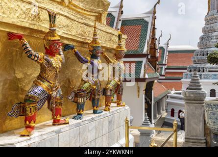 Un'immagine di statue alla base di un chedi dorato al Grand Palace di Bangkok Foto Stock