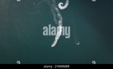 Vista aerea dall'alto in basso dell'avventura estiva in moto d'acqua che corre in giro per il giro, creando splendide onde bianche e spumeggianti sulla profonda superficie verde dell'oceano. Persone i turisti si rilassano, tempo libero, sport attivo Foto Stock