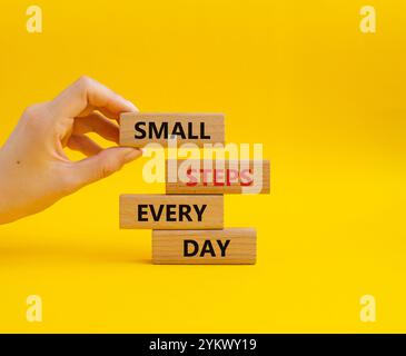 Simbolo piccoli passi ogni giorno. Blocchi di legno con parole piccoli passi ogni giorno. Bellissimo sfondo giallo. Mano d'affari. Business e piccoli passi Foto Stock